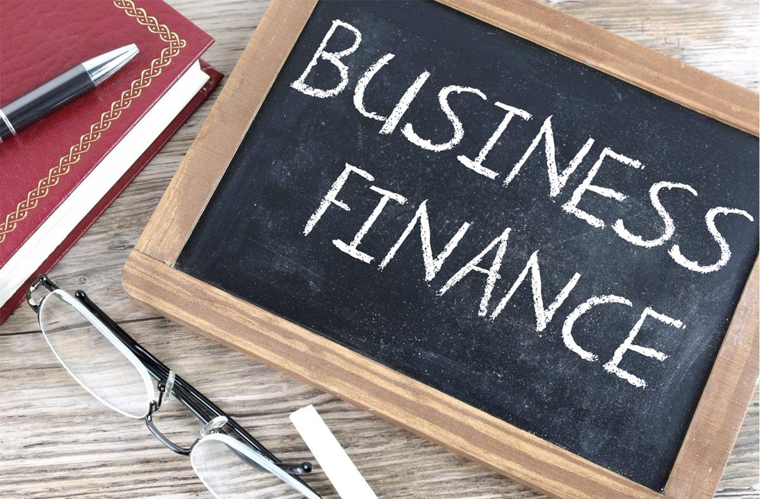 Liten griffeltavla med texten 'BUSINESS FINANCE' omgiven av kontorsmaterial.